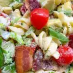 BLT pasta salad in a glass bowl with a side jar of ranch dressing and a green plaid towel