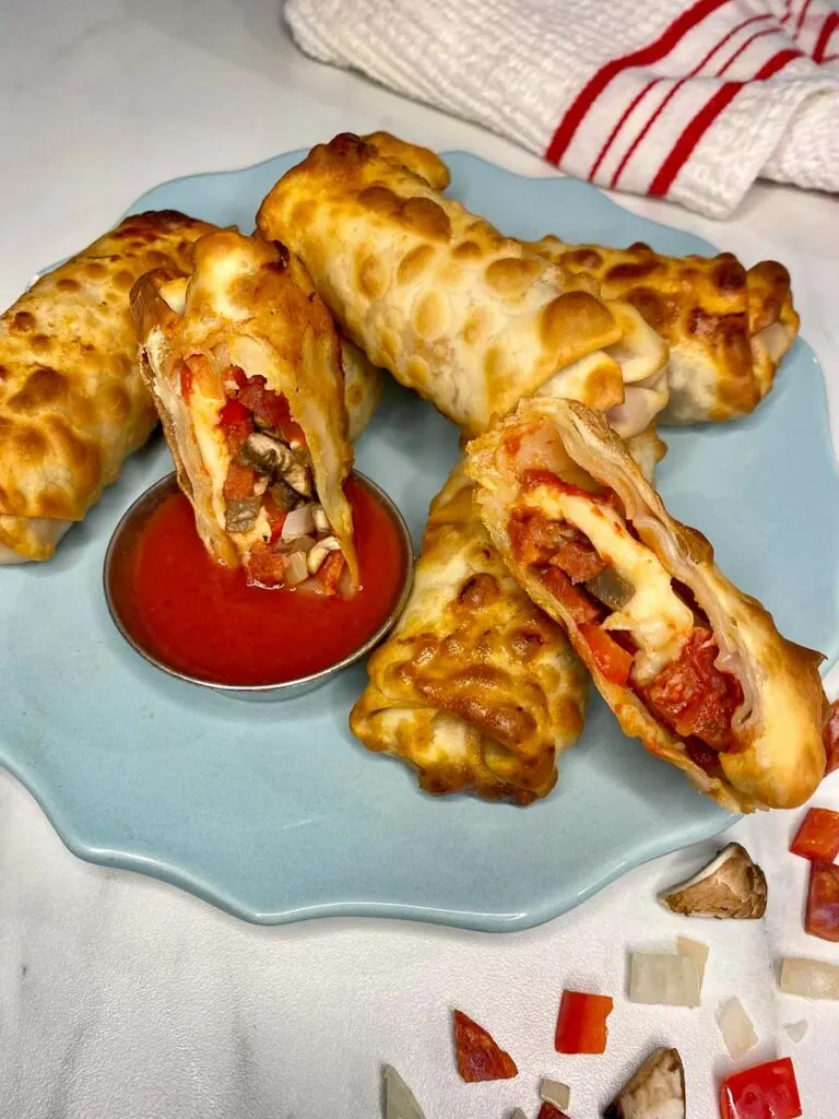 pizza egg rolls plated on a blue plate with pizza sauce to dip