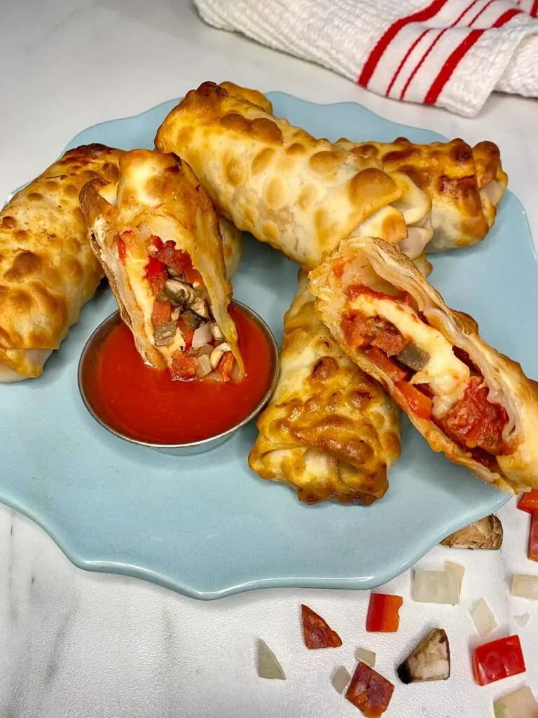 pizza egg rolls plated on a blue plate with pizza sauce to dip