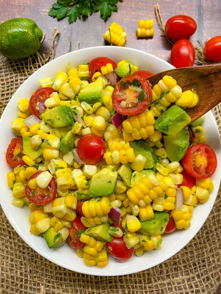 avocado corn tomato salad in a white bowl with burlap in the background