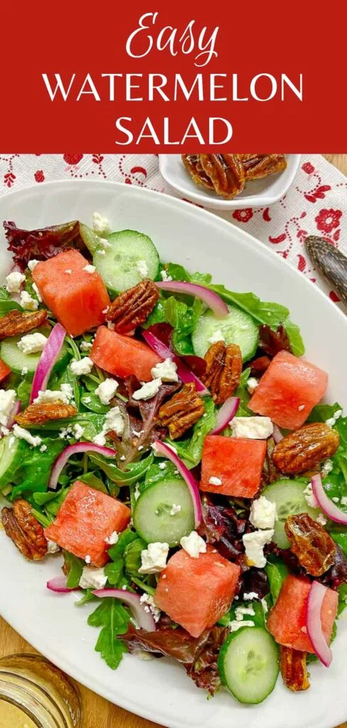 watermelon salad with feta cheese, candied pecans and red onion on a white platter