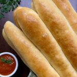 copycat olive garden breadsticks with a green checkerboard towel and marinara sauce to dip