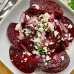 Greek beet salad garnished with crumbled feta cheese, pickled onions, parsley and oregano on a white plate