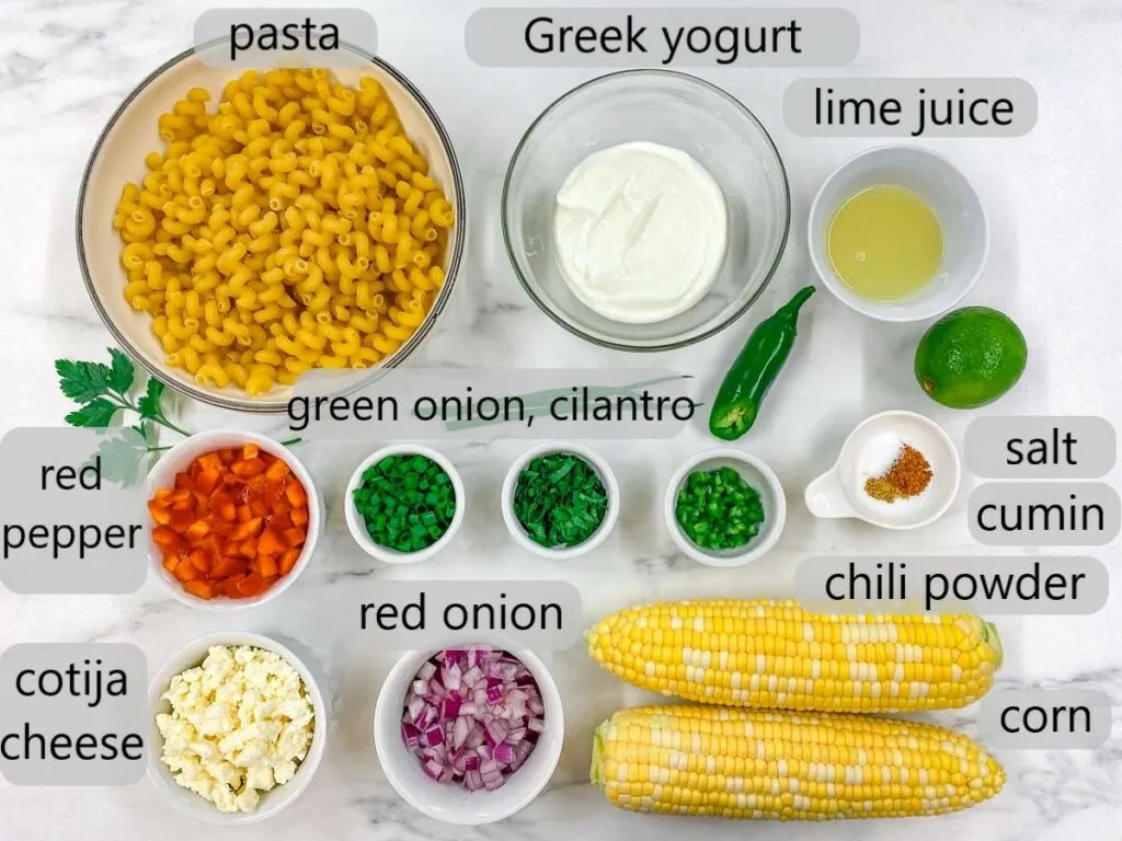 bowl with pasta, Greek yogurt, lime juice, red pepper, green onion, cilantro, jalapeno, salt, cumin, chili powder, cotija cheese, red onion and corn on the cob. The ingredients to make Mexican street corn pasta salad