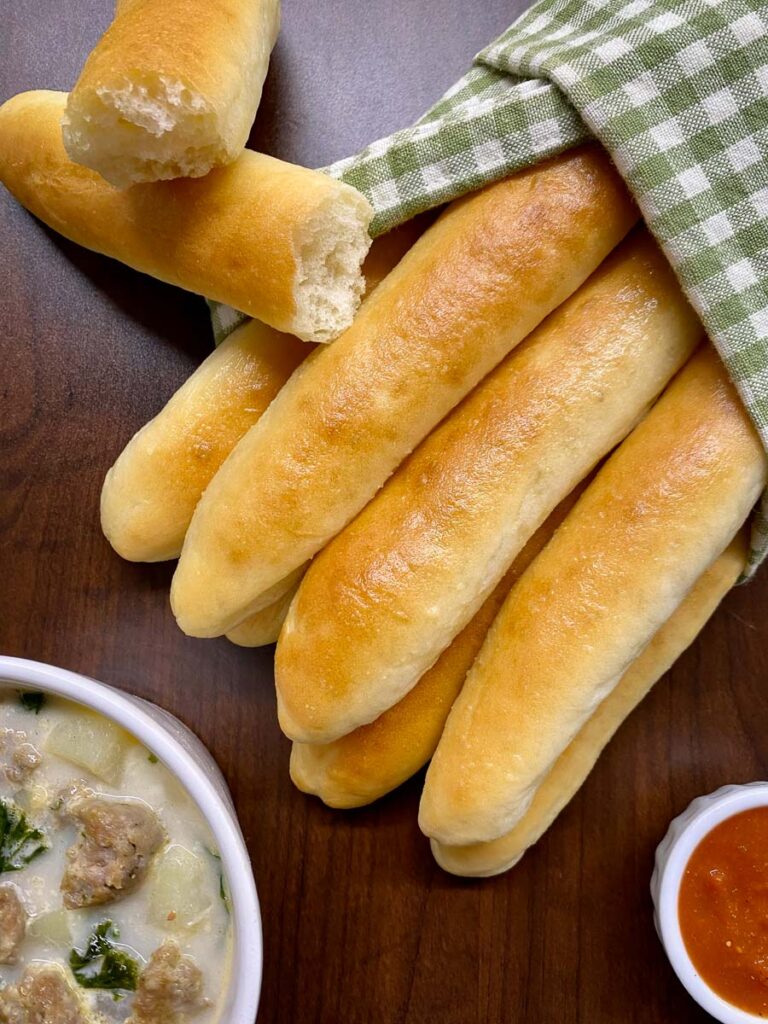 copycat olive garden breadsticks with a green checkerboard towel and marinara sauce to dip