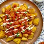 spanish patatash bravas on a brown platter garnished with tomato sauce, garlic aioli and parsley