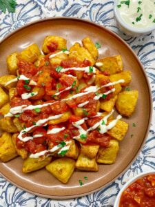 spanish patatash bravas on a brown platter garnished with tomato sauce, garlic aioli and parsley