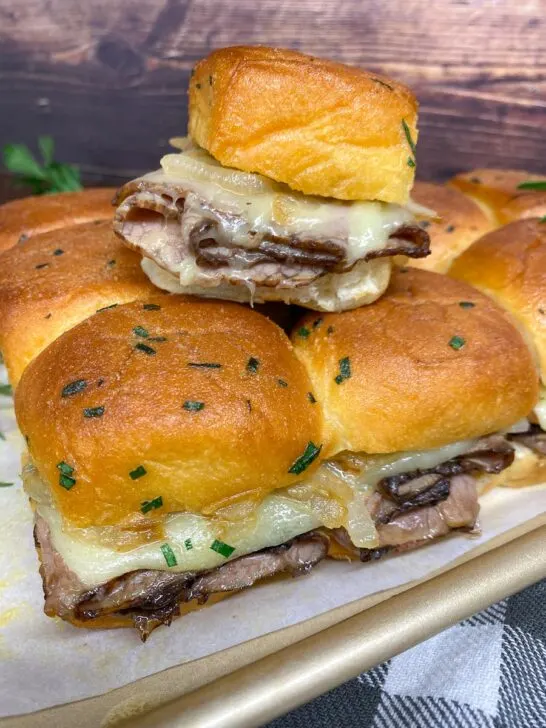 roast beef sliders with cheese and caramelized onions on a sheet pan garnished with rosemary