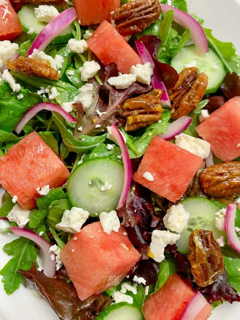 watermelon salad with feta cheese, candied pecans and red onion on a white platter