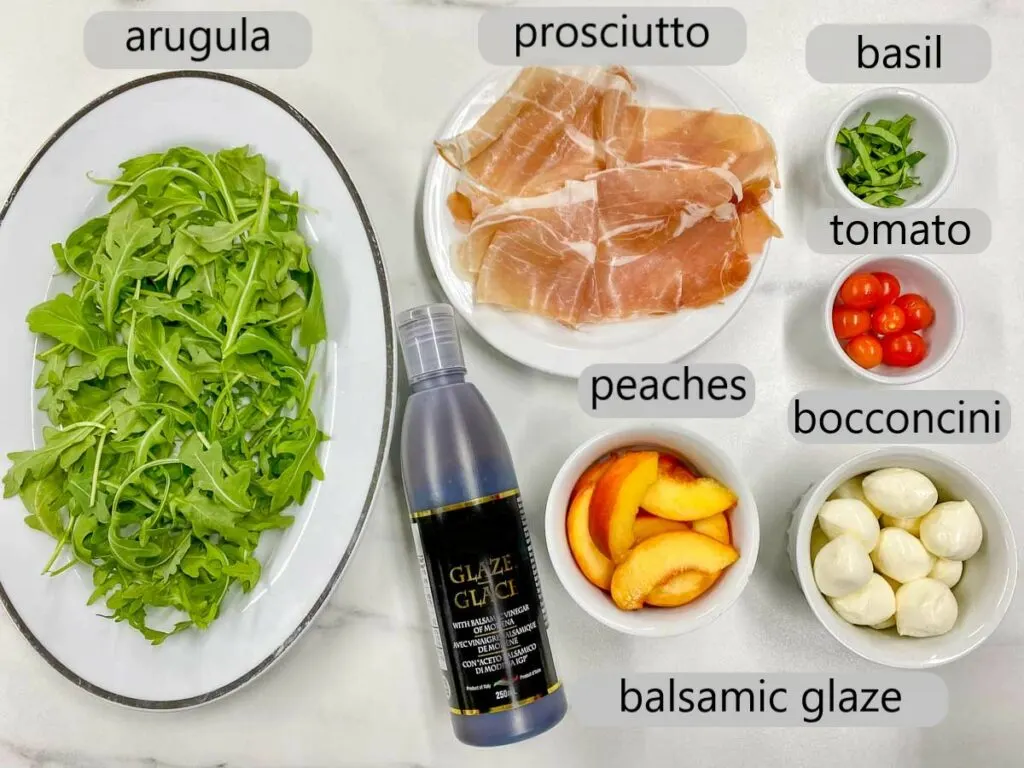 bowl with arugula, prosciutto, basil, tomato, bocconcini, peaches and balsamic glaze. the ingredients to make peach caprese salad