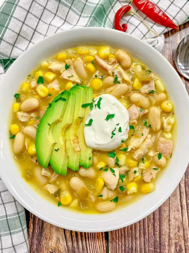 white chicken chili in a white bowl topped with avocado, sour cream and cilantro