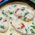 creamy Tuscan chicken in a cast iron frying pan garnished with sundried tomatoes and spinach