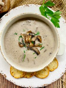 white bowl with cream of mushroom soup garnished with mushrooms and parsley