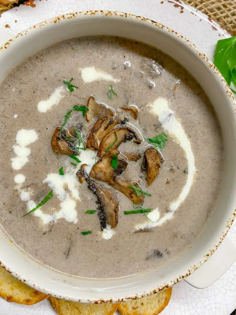 white bowl with cream of mushroom soup garnished with mushrooms and parsley