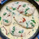 creamy Tuscan chicken in a cast iron frying pan garnished with sundried tomatoes and spinach