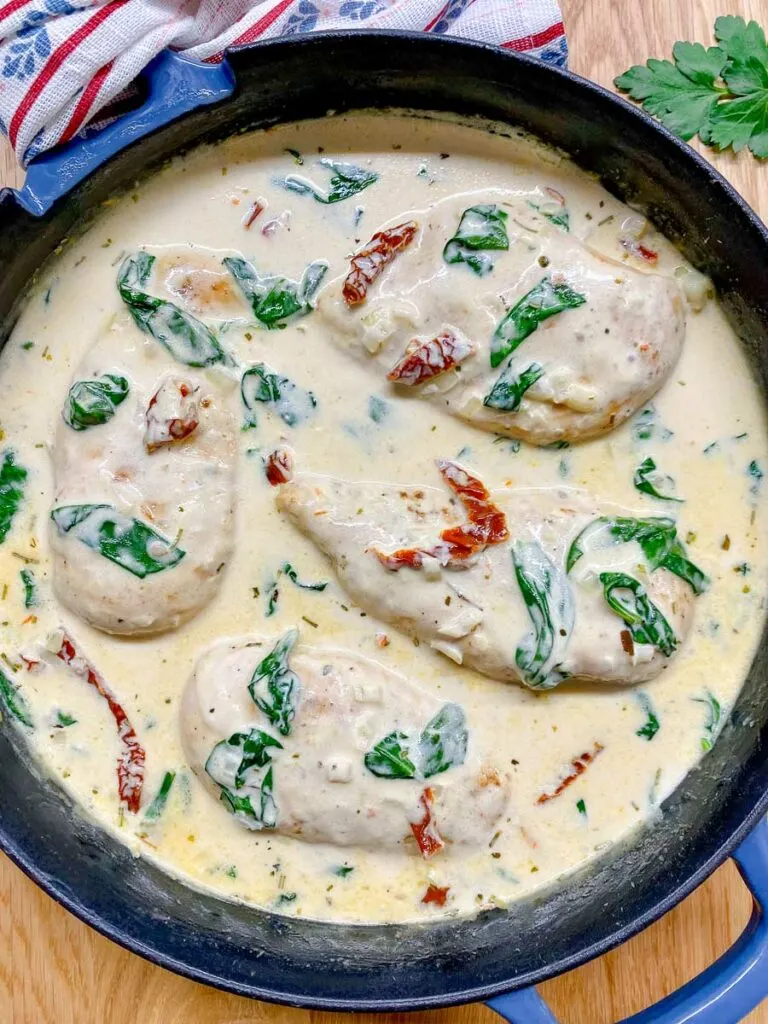 creamy Tuscan chicken in a cast iron frying pan garnished with sundried tomatoes and spinach