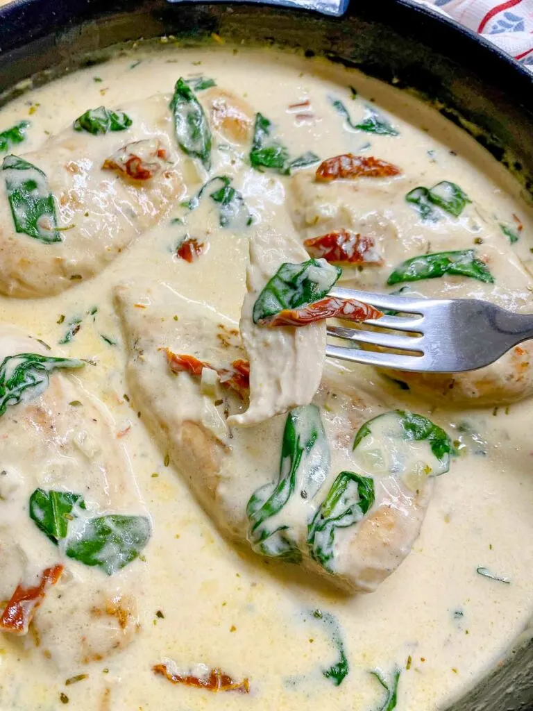 creamy Tuscan chicken in a cast iron frying pan garnished with sundried tomatoes and spinach