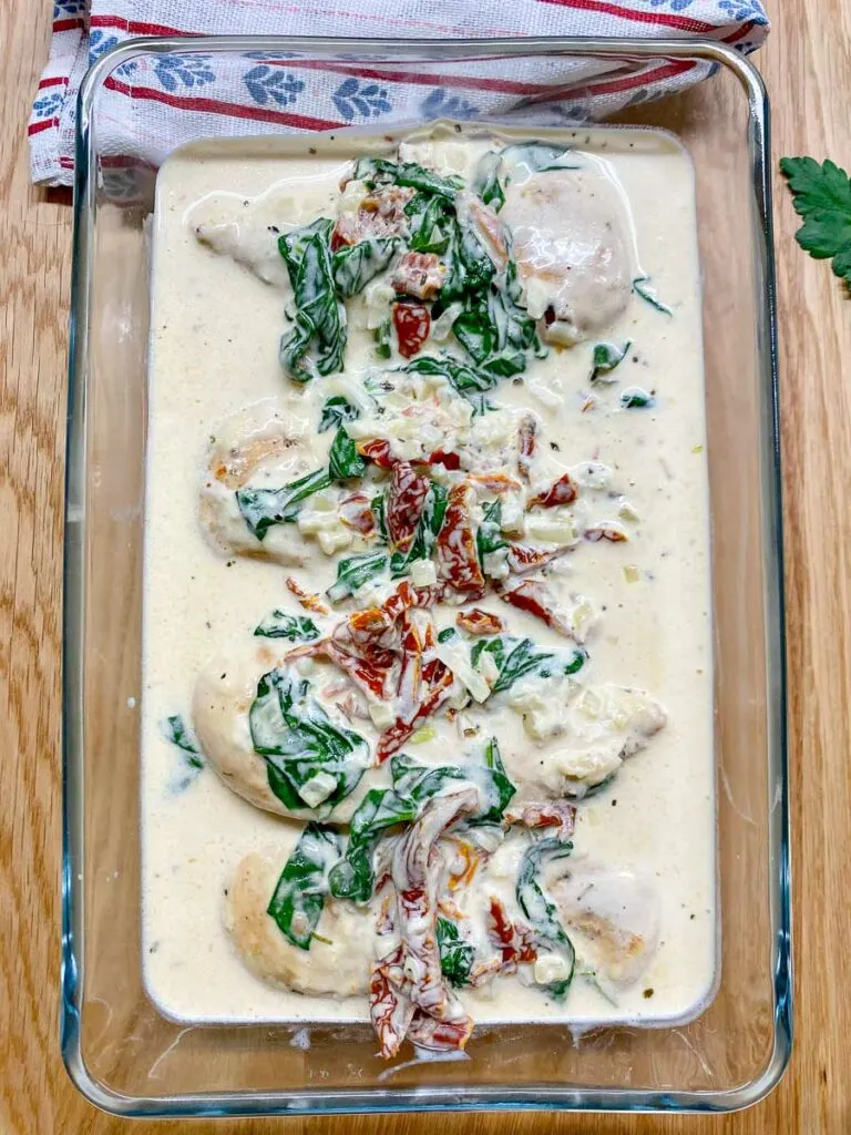 creamy Tuscan chicken in a glass baking dish garnished with sundried tomatoes and spinach