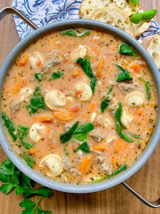 creamy tortellini soup in a pot with side of baguette