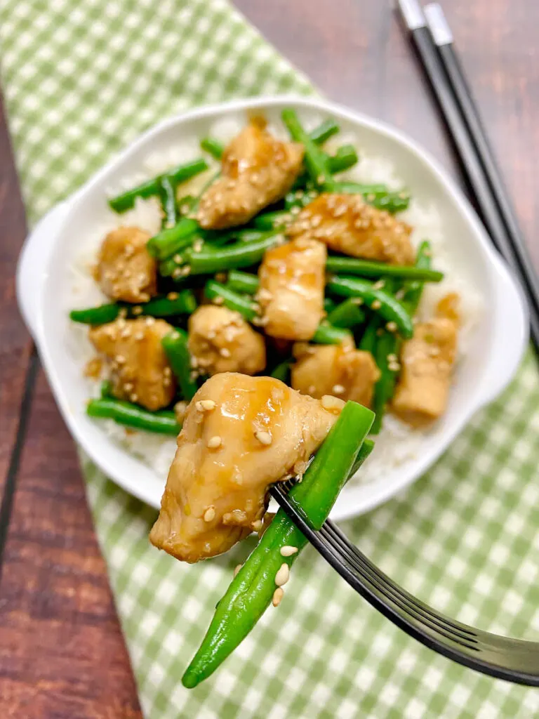 honey garlic chicken and green beans stir fry in a white bowl garnished with sesame seeds