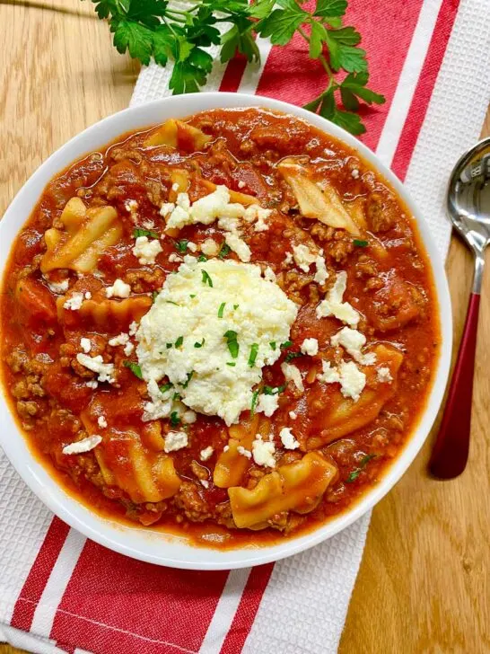 lasagna soup in a white bowl with ricotta cheese and fresh parsley