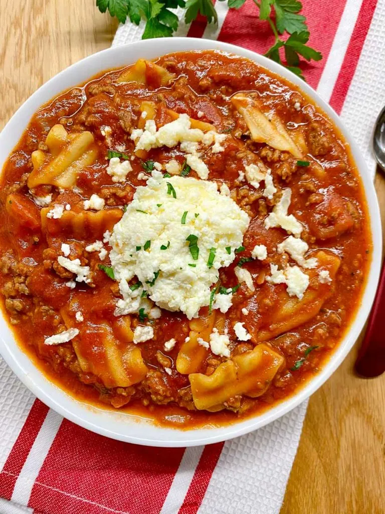 lasagna soup in a white bowl with ricotta cheese and fresh parsley