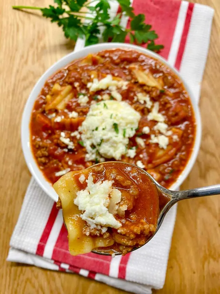lasagna soup in a white bowl with ricotta cheese and fresh parsley