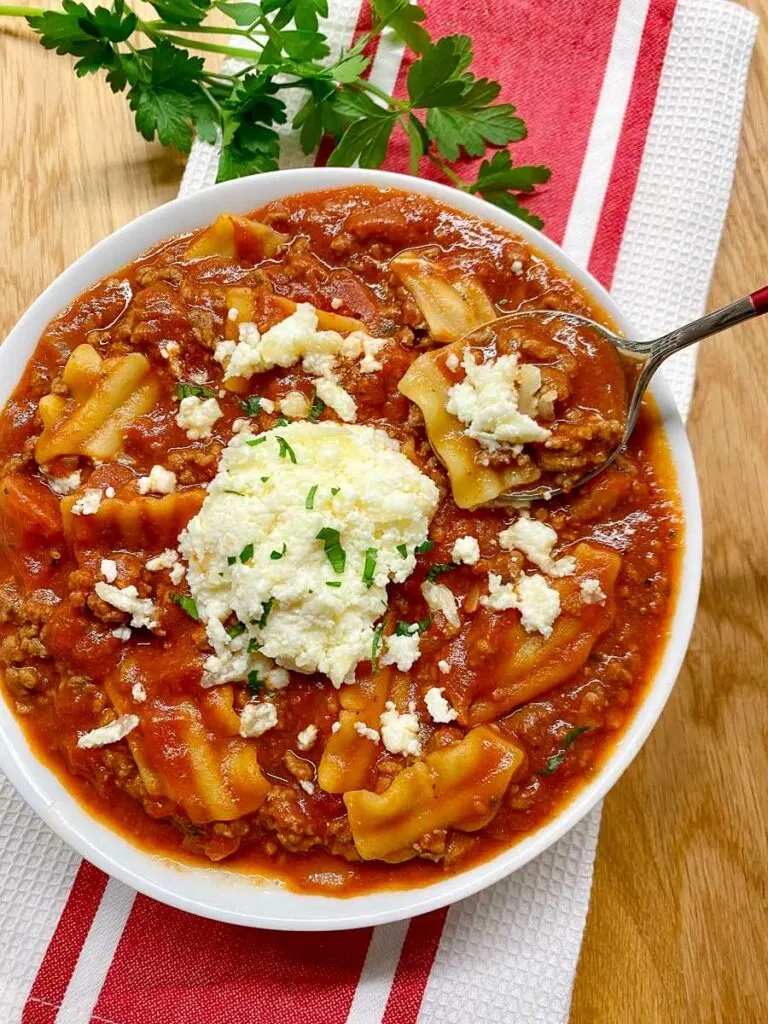 lasagna soup in a white bowl with ricotta cheese and fresh parsley
