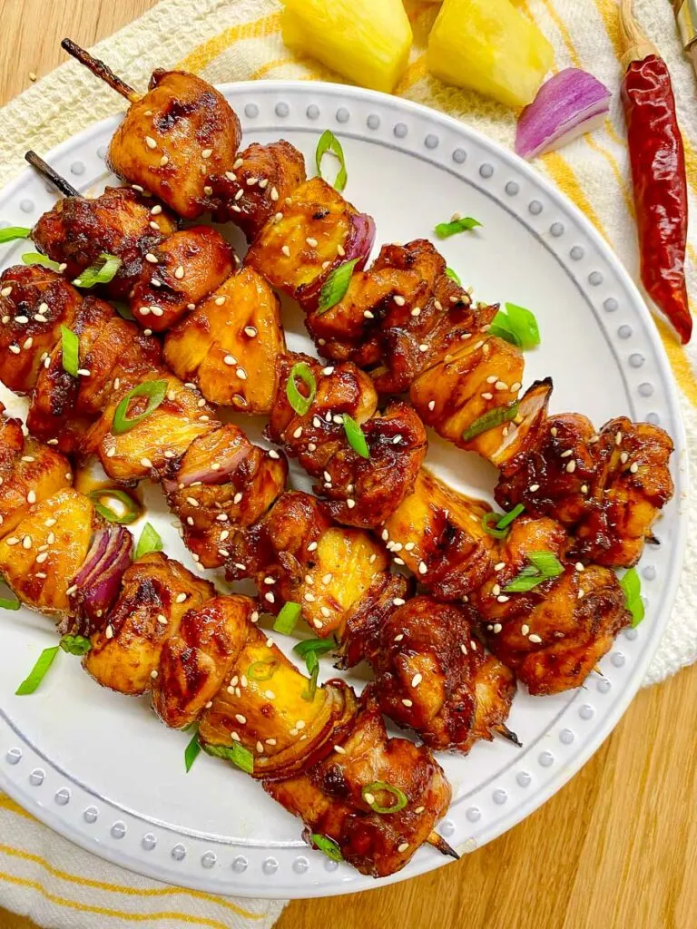 honey sriracha pineapple chicken skewers on a white plate garnished with green onions