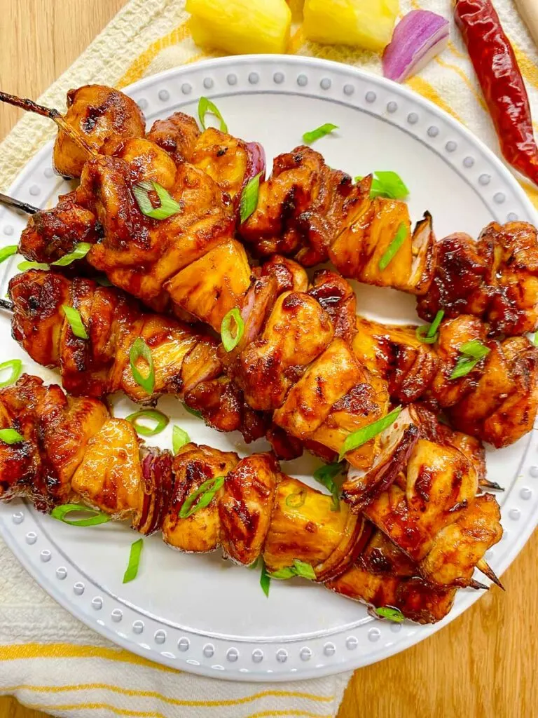 honey sriracha pineapple chicken skewers on a white plate garnished with green onions
