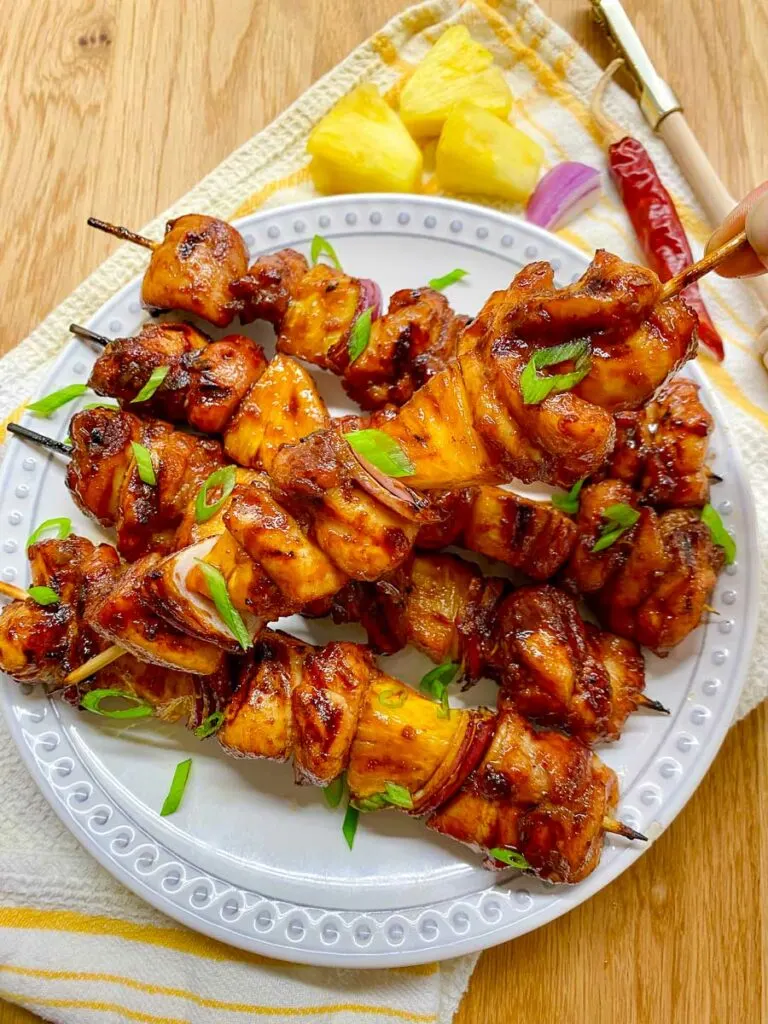 honey sriracha pineapple chicken skewers on a white plate garnished with green onions