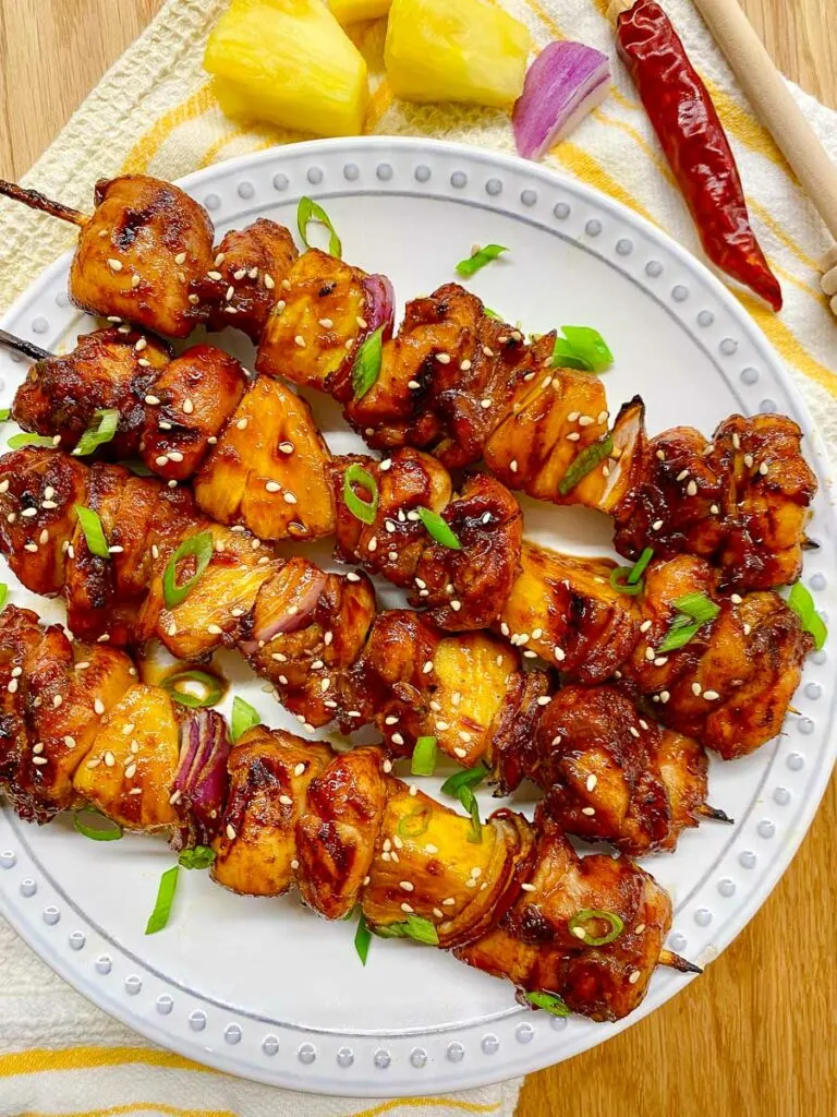 honey sriracha pineapple chicken skewers on a white plate garnished with green onions