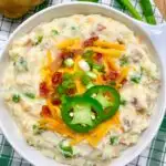 jalapeno popper mashed potatoes in a white bowl garnished with cheddar, bacon, green onion and jalapeno