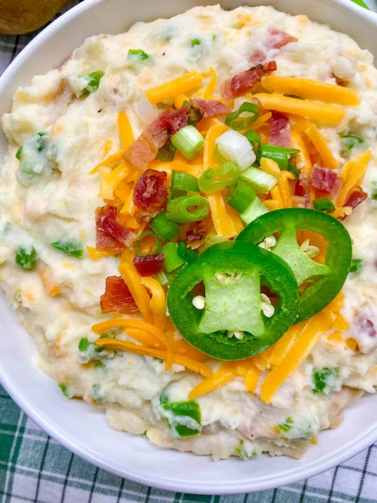 jalapeno popper mashed potatoes in a white bowl garnished with cheddar, bacon, green onion and jalapeno