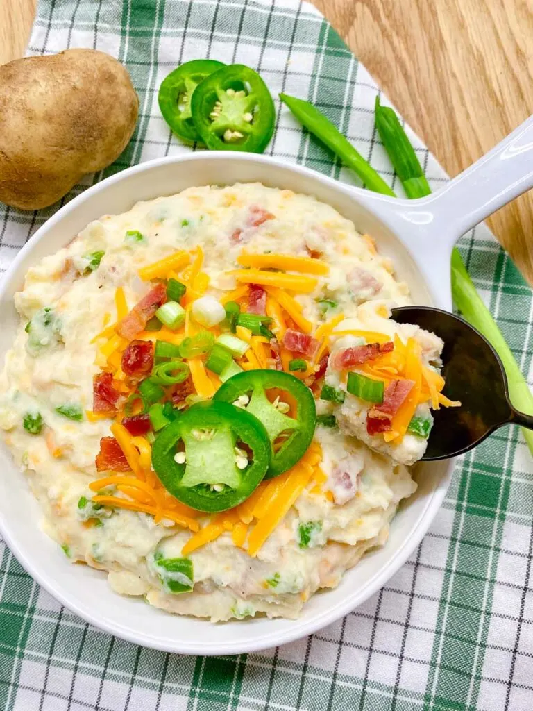 jalapeno popper mashed potatoes in a white bowl garnished with cheddar, bacon, green onion and jalapeno