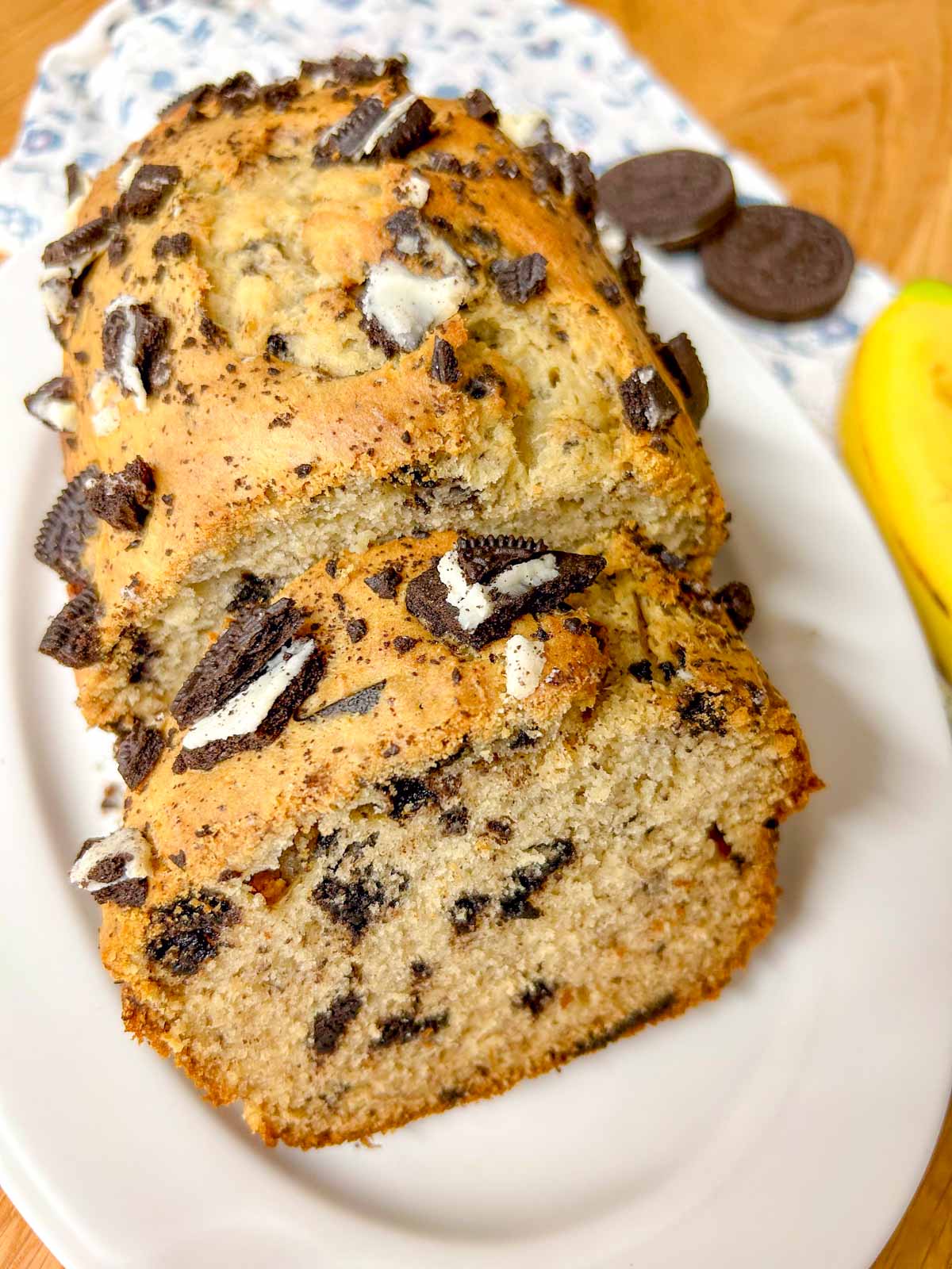 a loaf of Oreo banana bread is on a white serving platter. once piece of bread is sliced.