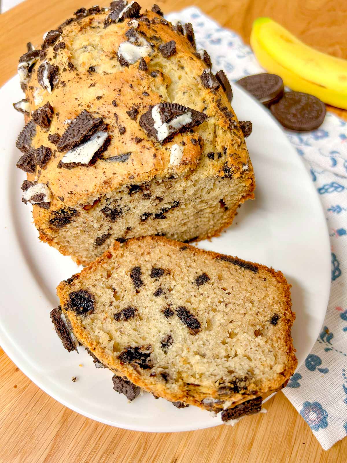 a loaf of Oreo banana bread is on a white serving platter. one piece of banana bread is sliced.