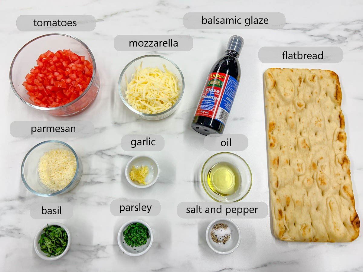a white marble counter top has the ingredients to make bruschetta flatbread pizza in bowls with text overlay reading - tomatoes, mozzarella, balsamic glaze, flatbread, parmesan, garlic, oil, basil, parsley, salt and pepper.