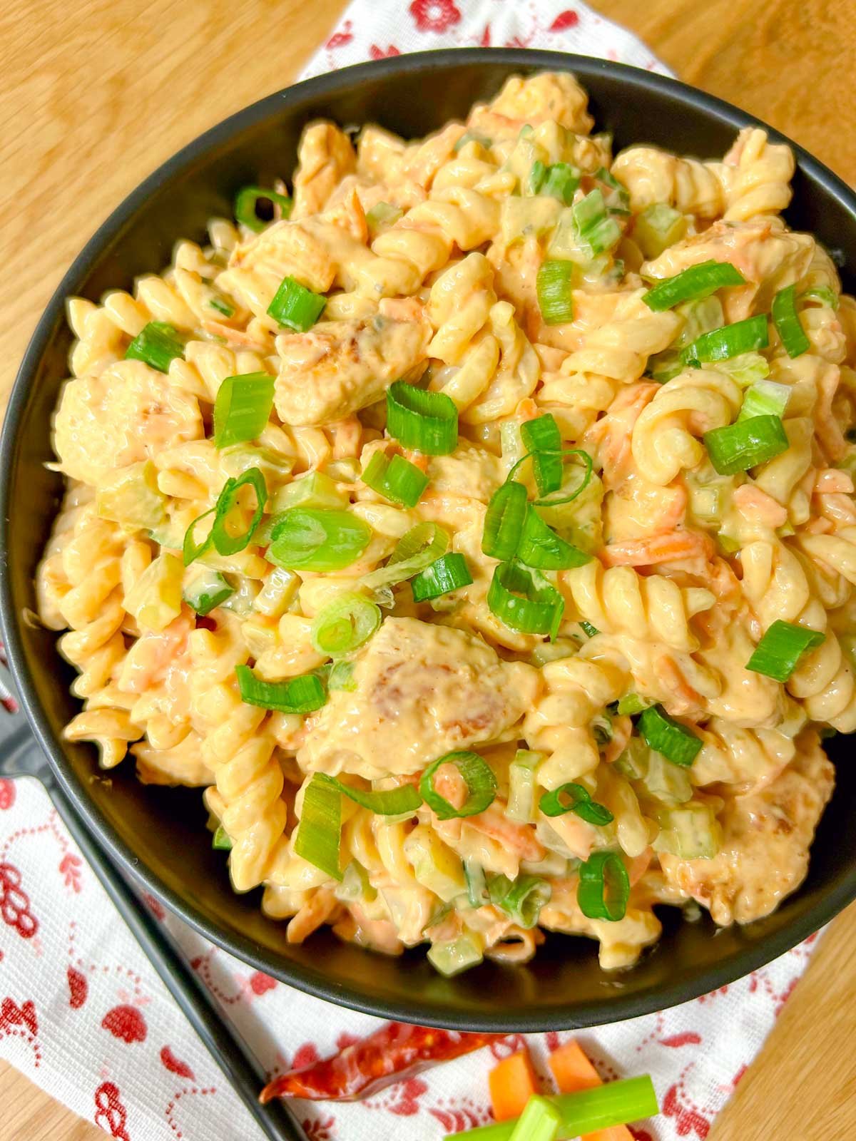 a black serving bowl is filled with buffalo chicken pasta salad and garnished with sliced green onions.