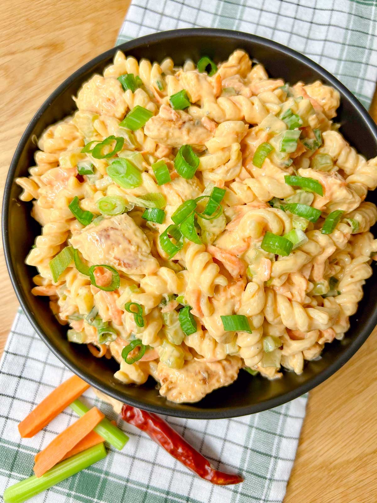 a black serving bowl is filled with buffalo chicken pasta salad and garnished with sliced green onions