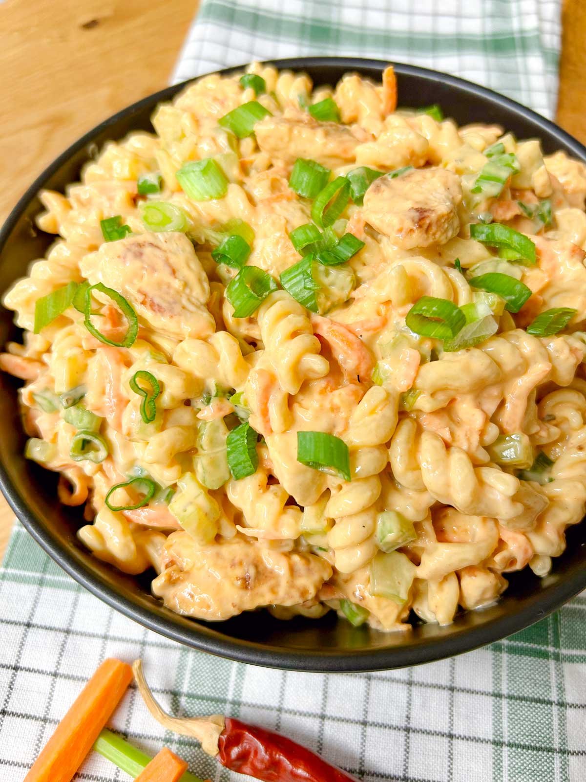 a black serving bowl is filled with buffalo chicken pasta salad and garnished with sliced green onions.