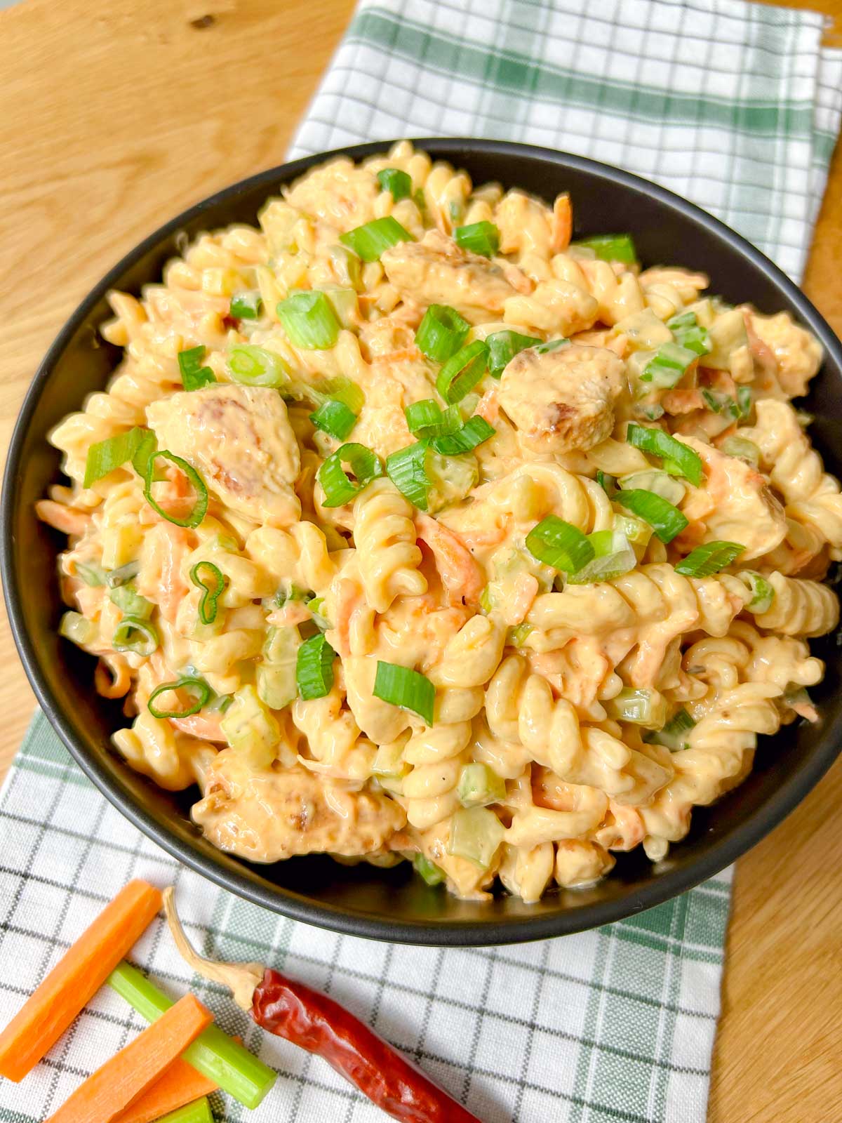 a black serving bowl is filled with buffalo chicken pasta salad and garnished with sliced green onions.
