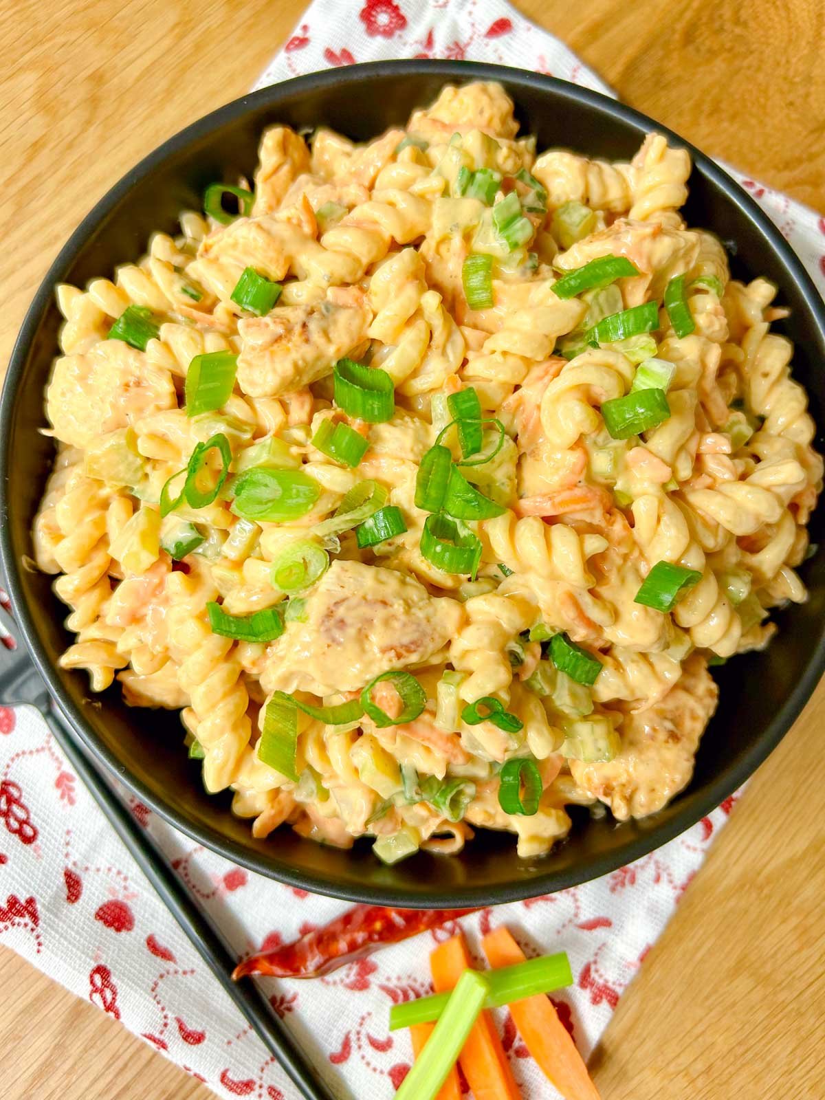 a black serving bowl is filled with buffalo chicken pasta salad and garnished with sliced green onions.