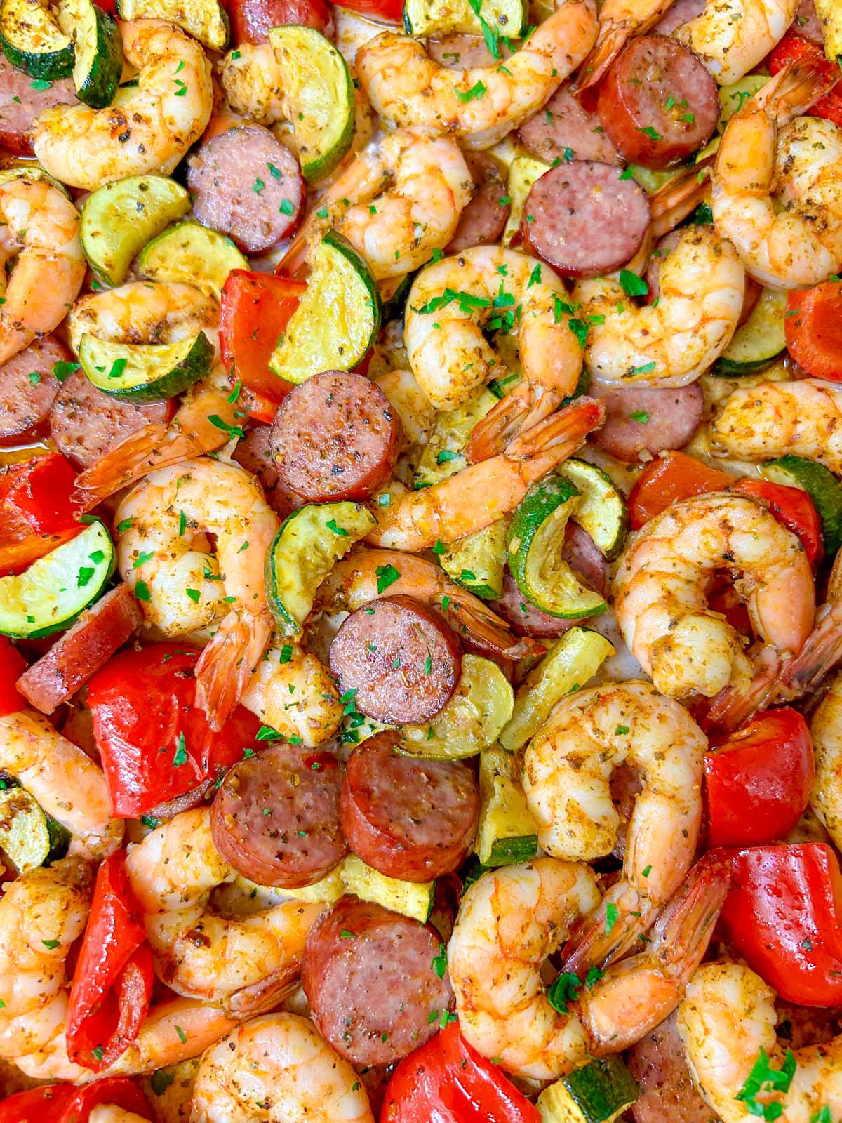 a white sheet pan is filled with a Cajun shrimp and sausage sheet pan bake on a wood counter top