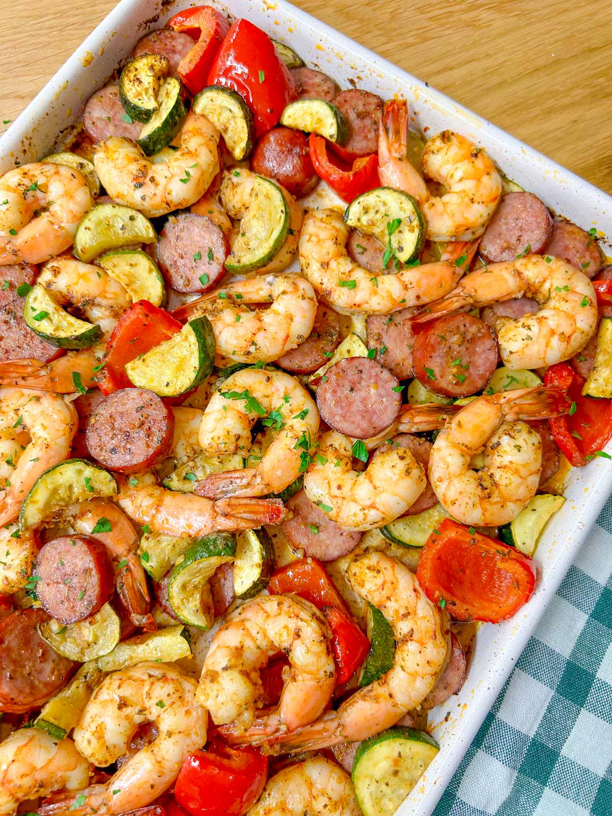 a white sheet pan is filled with a Cajun shrimp and sausage sheet pan bake on a wood counter top