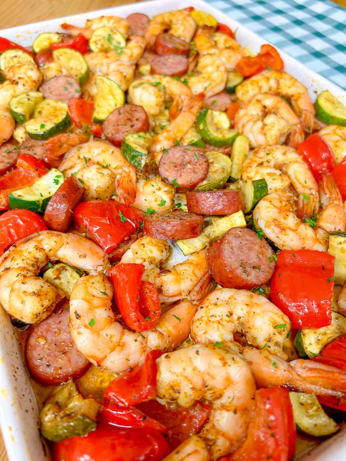 a white sheet pan is filled with a Cajun shrimp and sausage sheet pan bake on a wood counter top