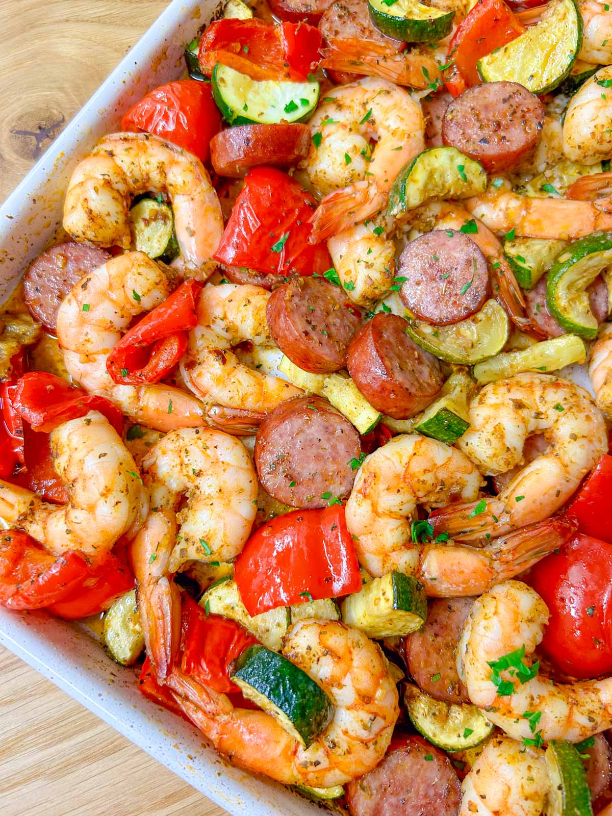 a white sheet pan is filled with a Cajun shrimp and sausage sheet pan bake on a wood counter top