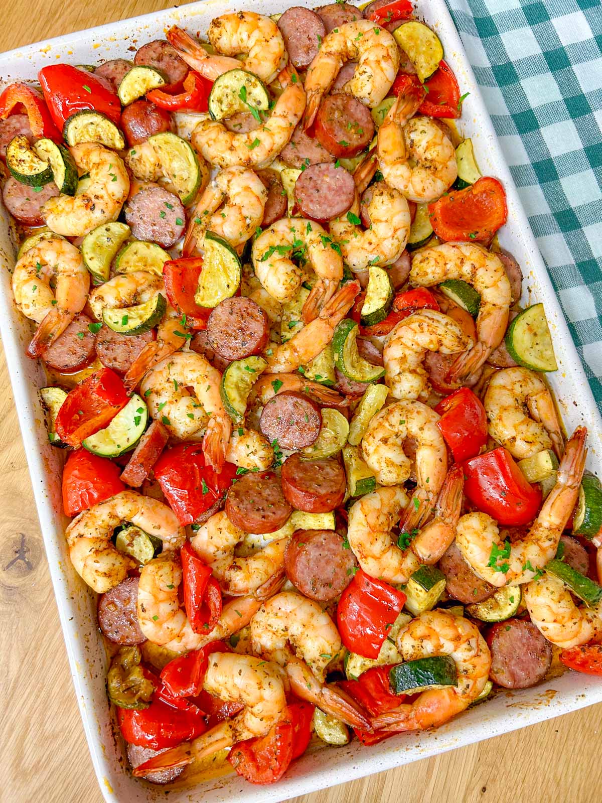 a white sheet pan is filled with a Cajun shrimp and sausage sheet pan bake on a wood counter top