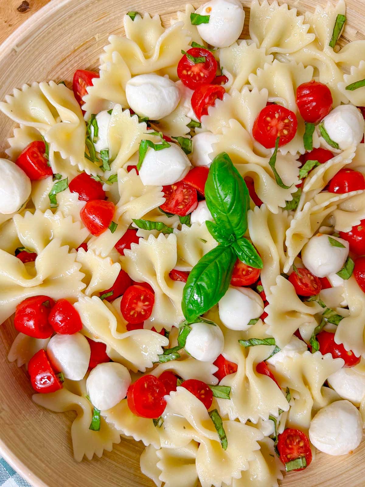 a wooden bowl is filled with caprese pasta salad and garnished with fresh basil