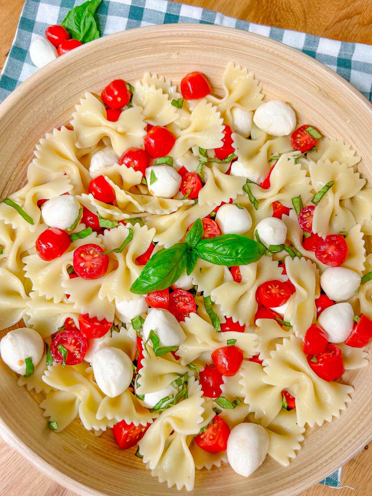 a wooden bowl is filled with caprese pasta salad and garnished with fresh basil